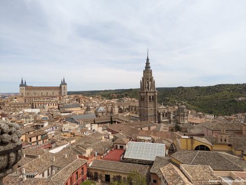 Em uma vista a partir do alto, temos uma série de telhados antigos. No meio da imagem, uma torre gótica de igreja; mais ao fundo, uma fortaleza militar com quatro torres.