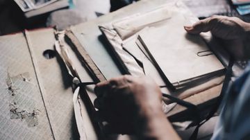 Duas mãos manuseam uma série de documentos e envelopes amarelados com o tempo.