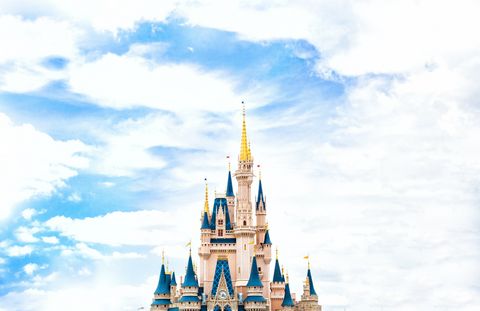 De fundo, um céu azul cheio de nuvens; em primeiro plano, a parte superior de um castelo claro, com o telhazo azul. A torre mais alta tem o telhado dourado.