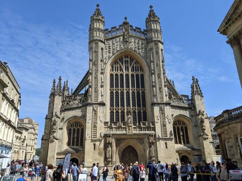 Em primeiro plano, um grupo grande de pessoas; ao fundo, uma imponente igreja em estilo gótico. O céu está azul e cheio de nuvens ralas.