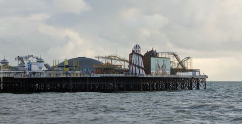 'Sobre um grande píer, vemos uma série de atrações d eum parque de diversões em estilo retrô, incluindo uma torre em espiral de escorregador e uma montanha-russa.'