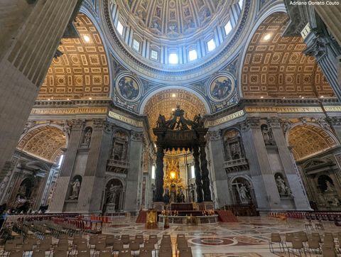 Vemos o interior de uma basílica, com o teto esculpido nas cores bege e marrom. Em cima, um domo com detalhes semelhantes. Ao centro, um altar com estrutura em bronze, composto de quatro colunas sinuosas e uma cobertura angulada.