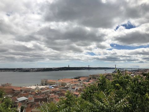 Do alto de uma colina, se avista um pouco de vegetação em primeiro plano, seguido de uma faixa cheia de casas, um rio de leito bem largo e mais uma faixa de terra.
