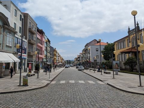 'Vista a partir do meio da rua, ladeada com construções portuguesas coloridas. O céu está azul com nuvens.'
