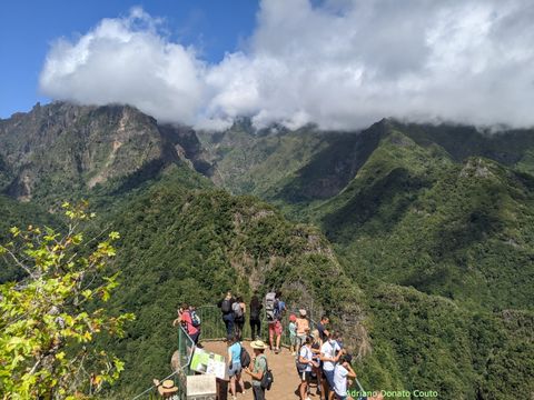 "Ao fundo, uma cadeia de montanhas; em primeiro plano, um miradouro com diversas pessoas."