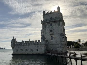 Uma torre quadrada bastante trabalhada no topo. Em um dos lados, um espaço murado. A torre está no meio de uma área alagada. Para chegar até ela, há uma travessia em madeira a partir do lado direito da imagem.