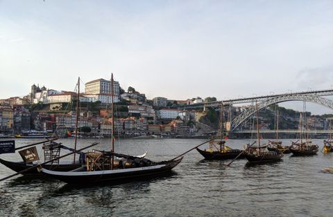 Vista a partir das margens do rio Douro, quase ao nível da água. Algumas embarcações em primeiro plano. Ao fundo, uma colina cheia de construções antigas.