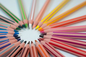 Lápis de cor de diferentes cores estão posicionados de forma que todos apontam para o centro, formando uma espécie de círculo.