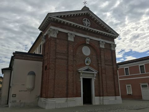 Ao fundo, o céu carregado de nuvens; à frente, uma igreja em tijolos vermelhos, com detalhes claros no topo e na base.