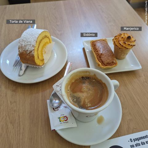 'Vista superior de uma mesa com um pedaço de torta que lembra rocambole, um doce marrom em formato retângulo e uma sobremesa em uma casquinha de sorvete em miniatura. Abaixo, temos uma xícara de café.'