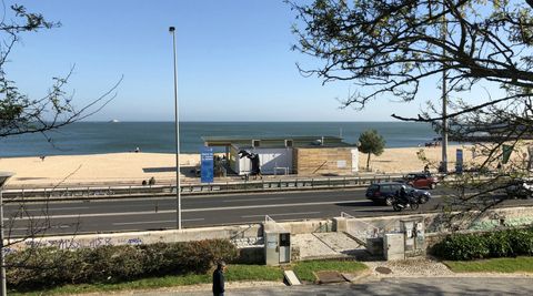 Em primeiro plano, uma pequena faixa gramada, depois uma via asfaltada e uma faixa de praia. No centro, um estabelecimento comercial.