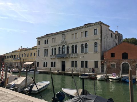 Em primeiro plano, vários barcos parados nas duas margens de um canal. Ao fundo, no centro da imagem, um prédio antigo de cor clara. É o Museu do Vidro, em Murano (Veneza).