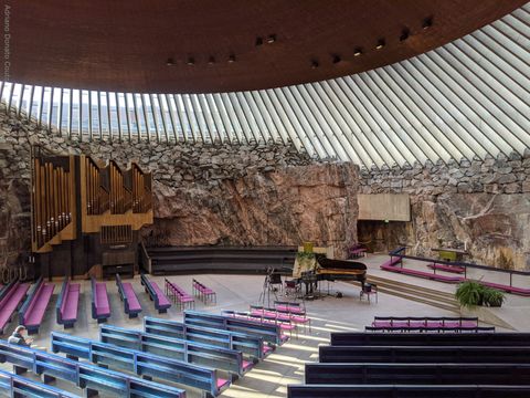 "Estamos no interior de uma igreja luterana. Em primeiro plano, fileiras de bancos de igreja rosas e azuis. Ao fundo, um órgão (instrumento musical) dourado, parede de pedra e um piano. O teto é de estrutura que mistura metal e vidro, com o topo central de cobre."