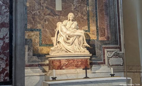 Na frente de uma parede coberta de mármores e granitos de diferentes cores, temos uma estátua clara de uma mulher entristecida, que segura um homem desacordado. São Maria e Jesus.