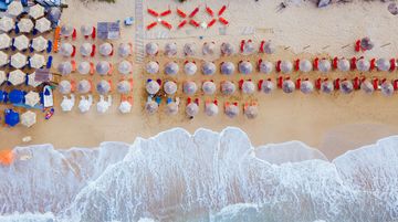 Na metade superior da imagem, uma faixa de areia (praia) com muitos guarda-sóis e cadeiras; na parte inferior, as ondas contra a costa.