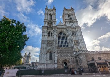 Sob um céu azul e cheio de nuvens, a fachada de uma igreja gótica com duas torres. Há uma árvore à esquerda.