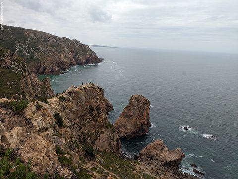 'À direita, temos um mar de um tom que fica entre verde e cinza. O céu está repleto de nuvens acinzentadas. À esquerda, um linha tortuosa de penhascos de diferentes alturas.'
