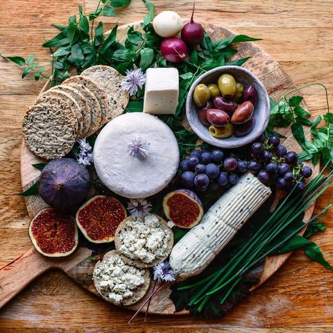 Tábua com biscoito salgado, azeitonas, rodelas de figo folhas e versões veganas de queijo.
