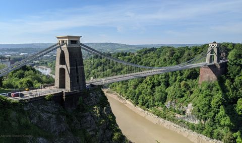 Ponte suspensa sobre um profundo leito de rio, o rio Avon. Nas margens, extensa área de mata.
