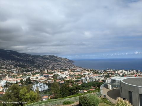 "Vista aérea, do alto de um morro, com uma colina repleta de casas à esquerda; à direita, o mar; e acima, um céu carregado de nuvens acinzentadas."