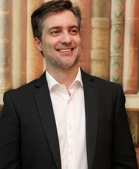 Daniel Taddone, homem branco de cabelos já um pouco grisalhos, sorri olhando para o canto direito da imagem.