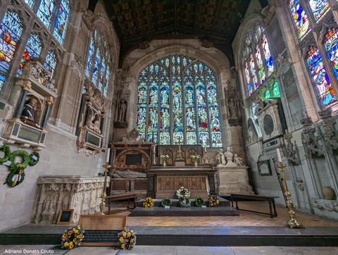 Vemos o interior de uma igreja antiga, com enormes vitrais coloridos. À esquerda, temos um busto colorido de William Shakespeare.