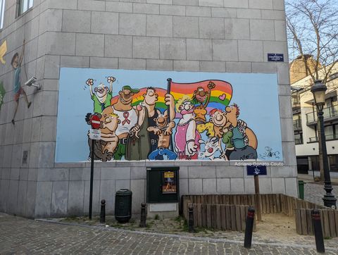 Em uma parede cinza, um painel colorida traz um desenho de diferentes pessoas do coletivo LGBT em uma parada do Orgulho.