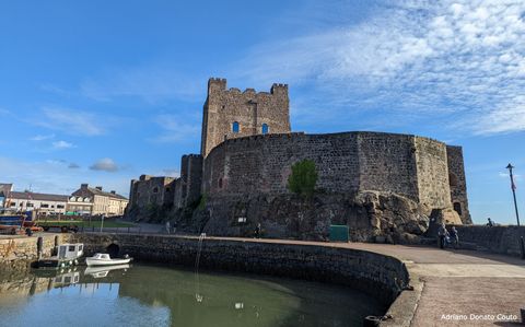 Sob um céu azul, um caminho de concreto leva às ruínas de um castelo de pedra.