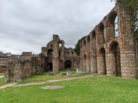 Grande área de grama, ladeada por colunas e arcos de pedra, que compõem as ruínas de um antigo monastério.
