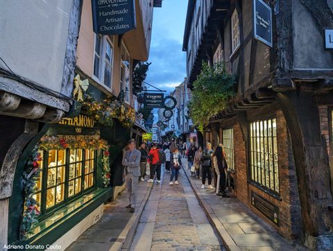 Uma rua estreita, com construções com aparência medieval, com estrutura de toras de madeira. O dia está nublado e escuro.
