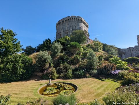 Em primeiro plano, uma pequena lagoa rodeada por um jardim. Ao fundo, uma pequena colina que leva a uma torre circular de pedra.