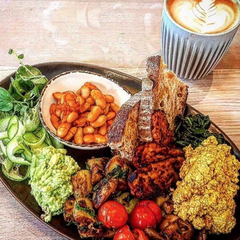 Um prato com torradas, tomate, pasta de avocado e algumas opções veganas que simulam ovos mexidos e outras proteínas.