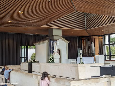 Sob um teto de madeira, temos uma pequena capela branca com teto de telha de barro e, em frente, um pedestal com uma imagem de Nossa Senhora no topo.
