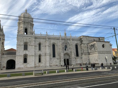 Uma igreja toda em cor clara, com uma longa porta dupla ao centro e várias janelas alongadas em sua fachada. Do lado esquerdo, a construção sobe em uma espécie de torre, com cúpula toda esculpida e também em tom claro.