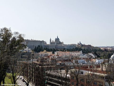 Sob um céu azul claro, vê-se ao fundo um palácio antigo e uma catedral azul claro. Em primeiro plano, várias construções e árvores sem folhas.