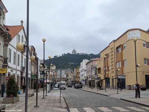Sob um céu nublado, em rua ladeada por construções antigas de uma rua de pedra, vemos ao fundo um monte verde com uma igreja no topo.